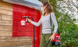 Pistola a spruzzo EINHELL mentre vernicia una casetta in legno