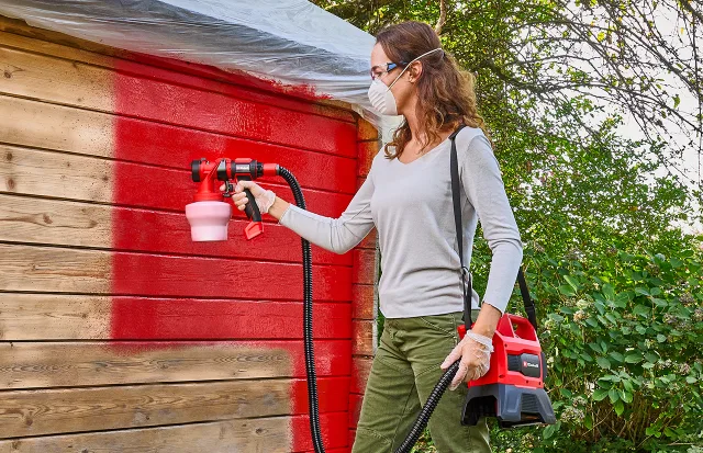 Pistola a spruzzo EINHELL mentre vernicia una casetta in legno